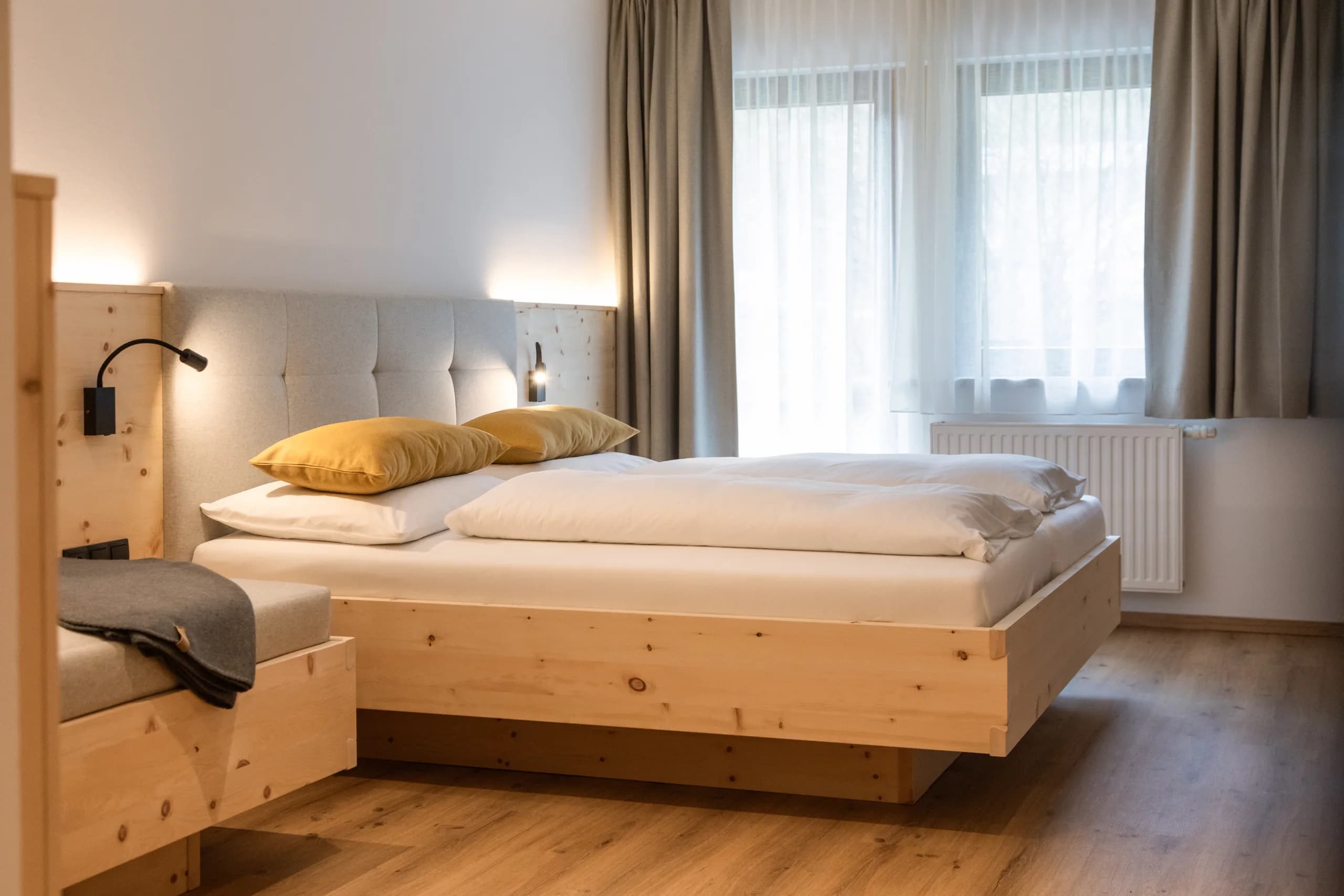 Gemütliches Bett aus hellem Holz mit gepolstertem Kopfteil im Zimmer Freiraum der Natur Residenz Anger Alm